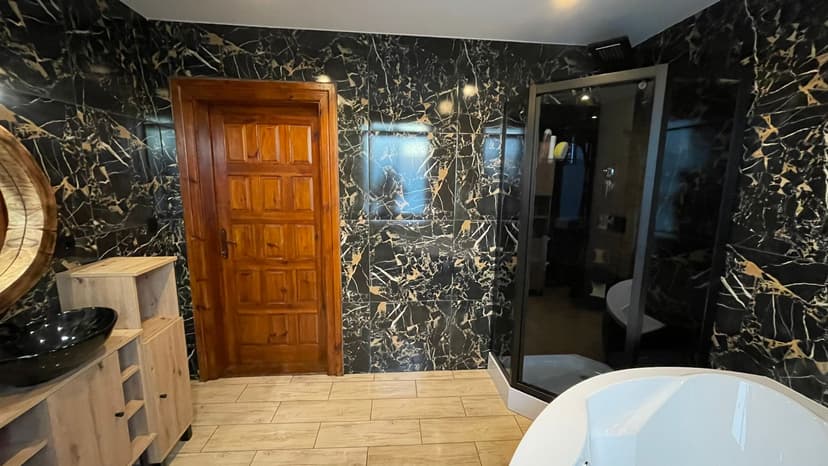 Łazienka z antracytową kabiną prysznicową, płytki o fakturze ciemnego marmuru, płytki podłogowe o jasnej kolorystyce.