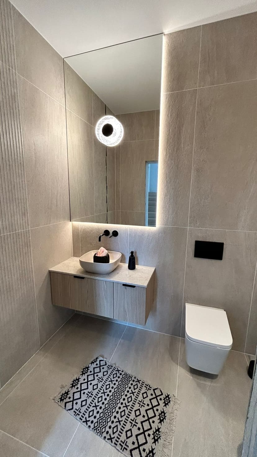 Toaleta z dużym podświetlanym lustrem, białą umywalką, płytki wielkoformatowe na ścianach w kolorze jasnego piaskowca