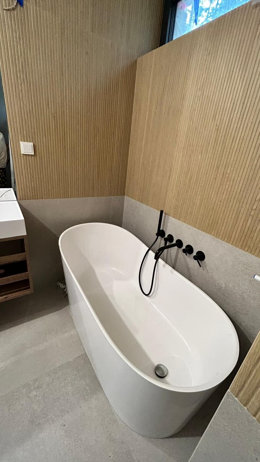 Łazienka z płytkami perforowanymi o kolorze piaskowym, wanna stojąca z czarną armaturą i beżowymi płytkami do wysokości wanny.