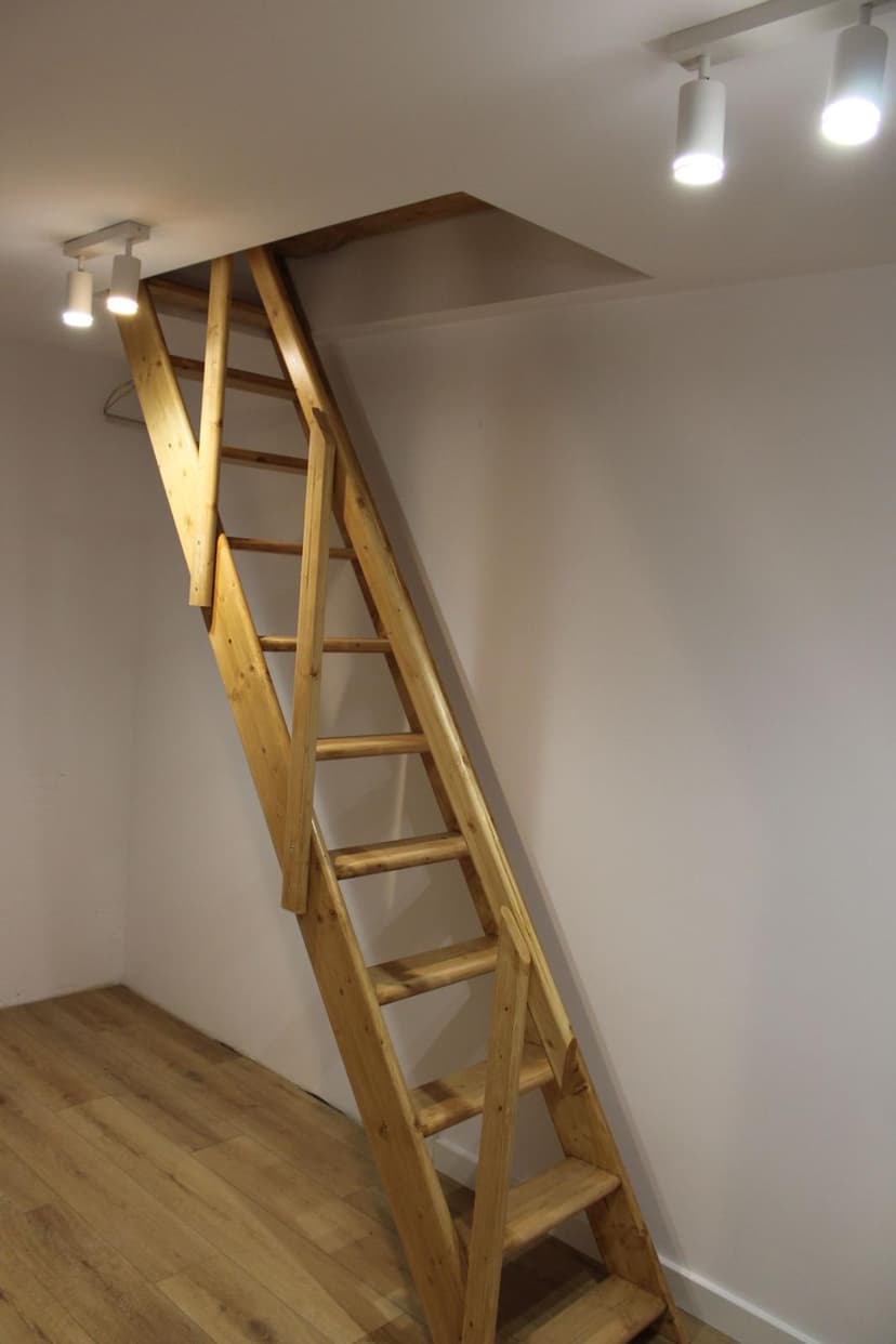 Schody wejściowe na antresolę, jasne ściany i oświetlenie puntkowe w kolorze białym.